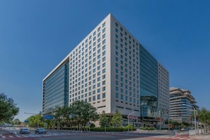 A modern high-rise building with a glass facade, located at a city intersection.