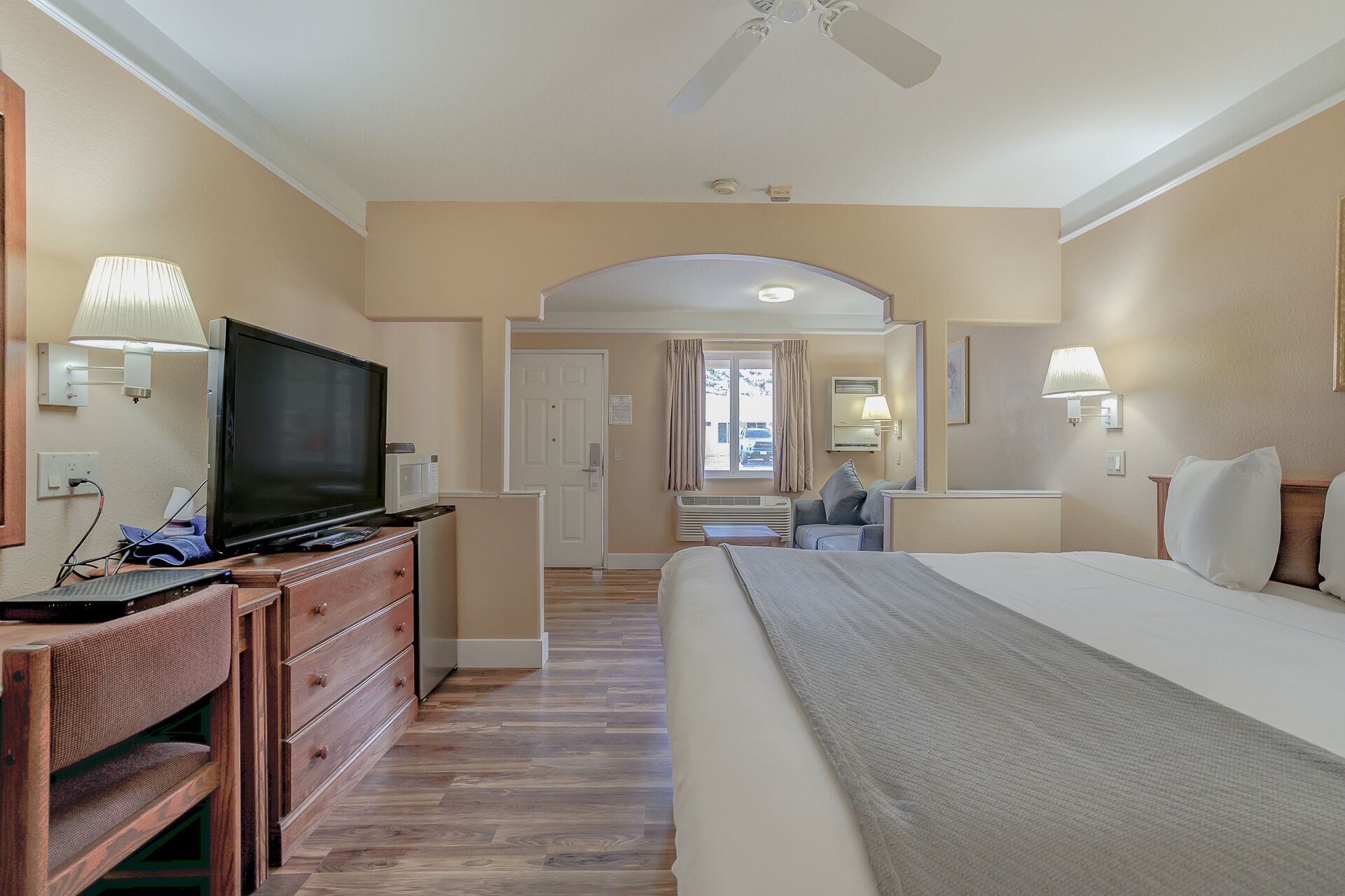 A hotel room with a bed, a desk with a television, a dresser, and a mirror.
