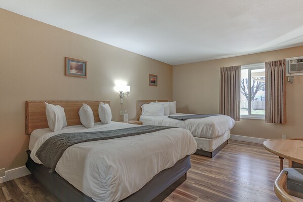 A hotel room with two beds, a small table, and a window with curtains.