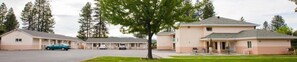 A motel with a parking lot, a covered picnic area, and a building with a sloped roof. - Shasta Pines Motel & Suites (Burney)