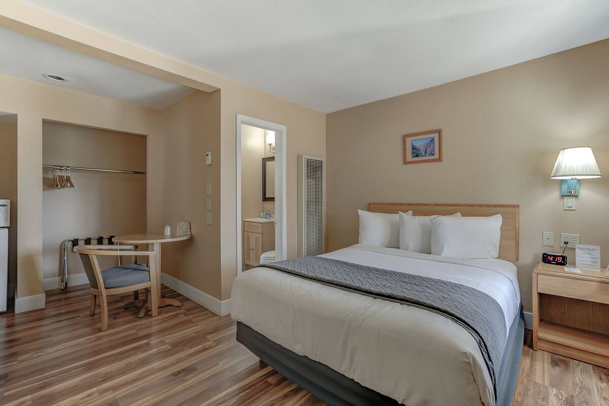 A hotel room with a bed, bedside table, lamp, and a desk with a chair.