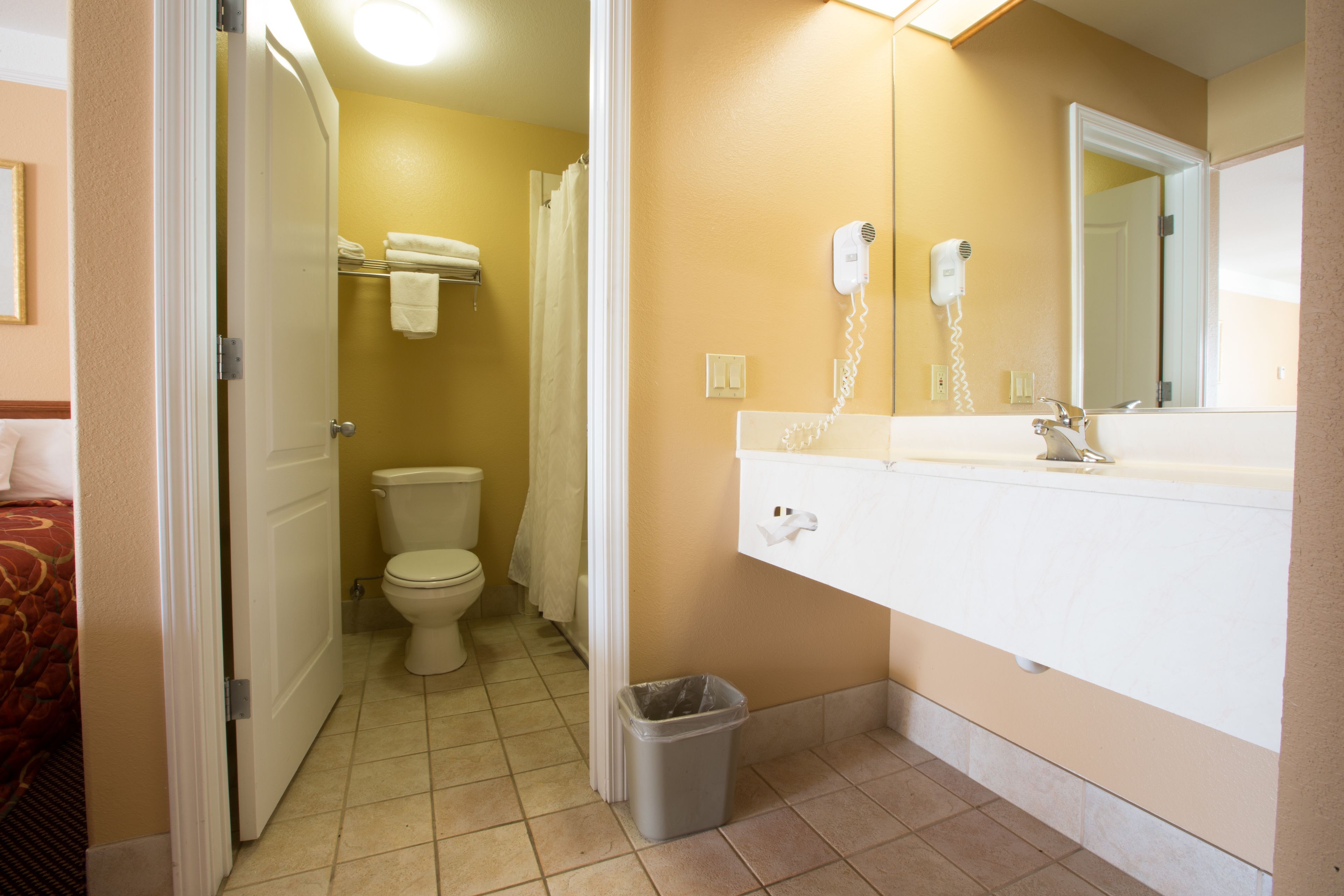 A bathroom with a toilet, a shower curtain, a hairdryer, and a trash bin.