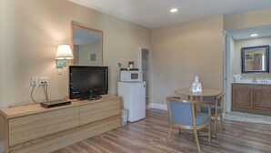 A hotel room with a wooden cabinet, a flat-screen TV, a microwave, a small refrigerator, a dining table with two chairs, and a bathroom visible through an open door. - Shasta Pines Motel & Suites (Burney)