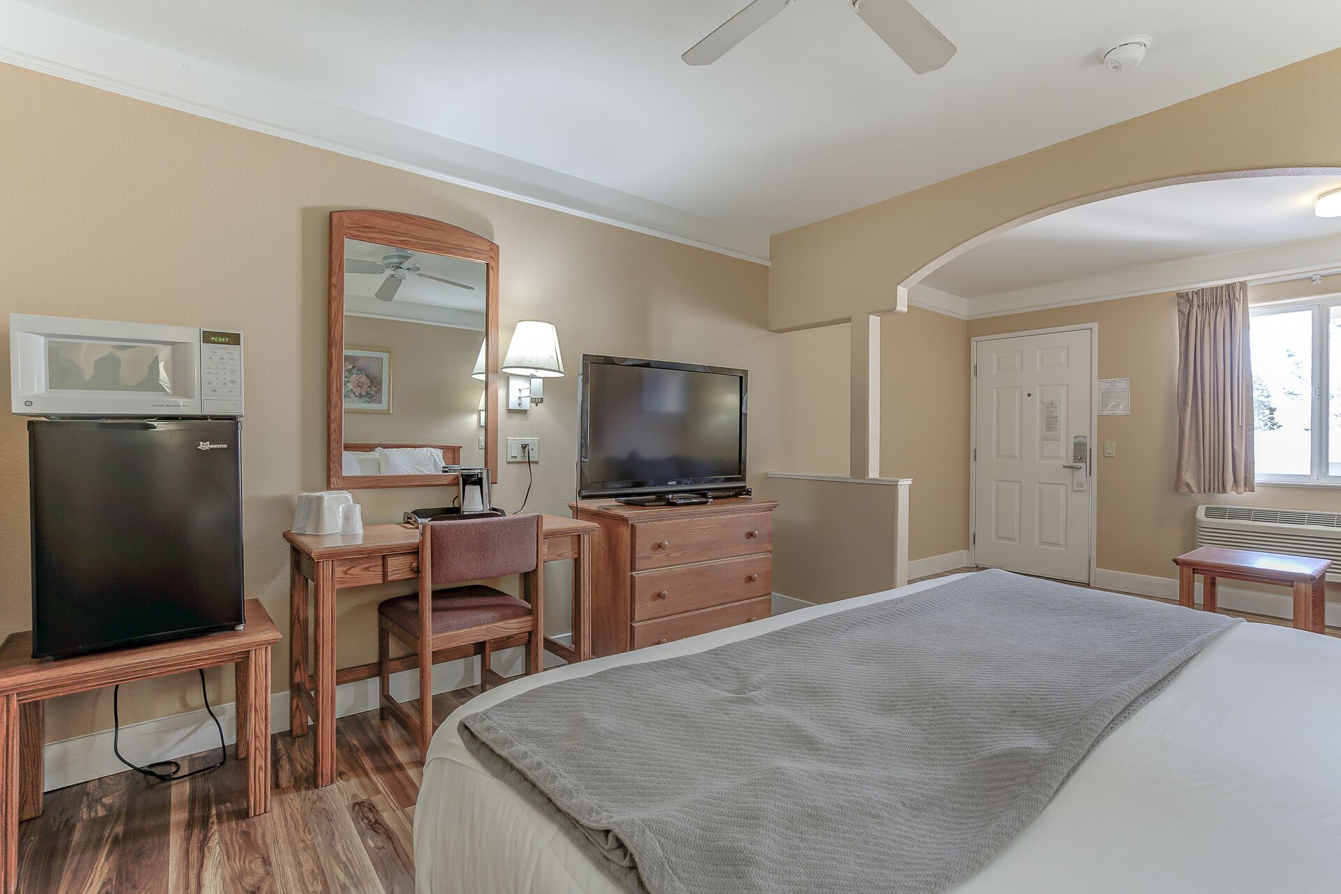 Una habitación de hotel con una cama, un escritorio con una silla, un televisor, un microondas y un refrigerador.
