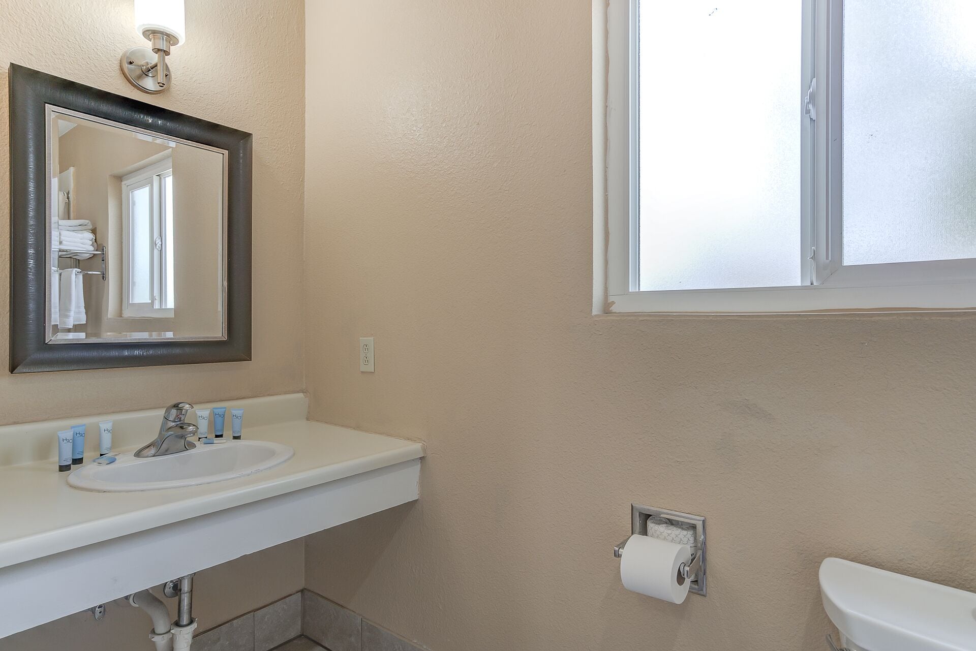 Une salle de bain avec un lavabo blanc, un miroir, des toilettes et une fenêtre.