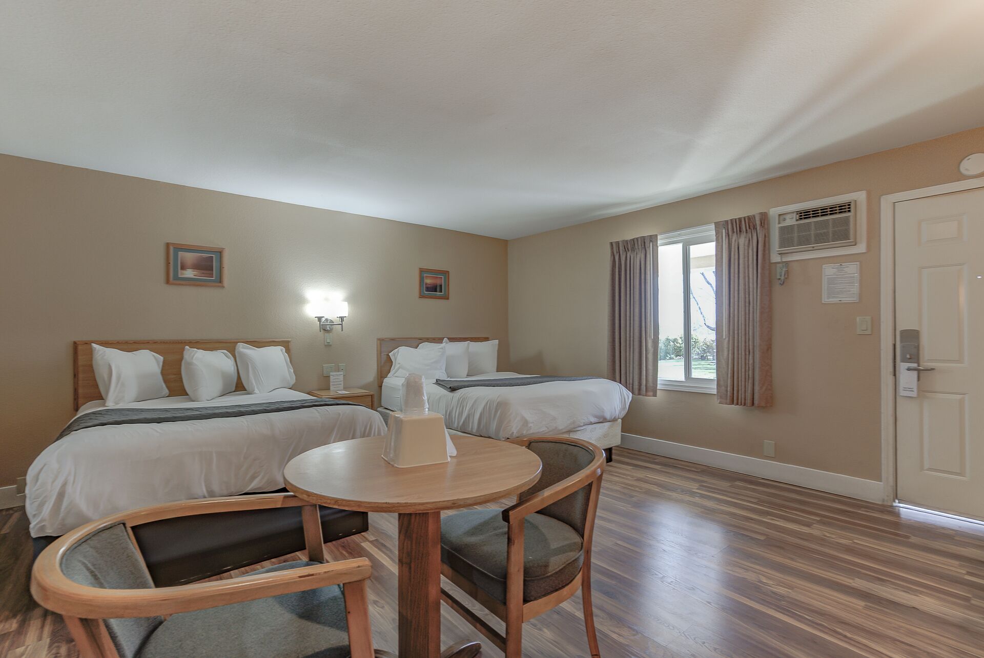 A hotel room with two beds, a small round table, and a chair.