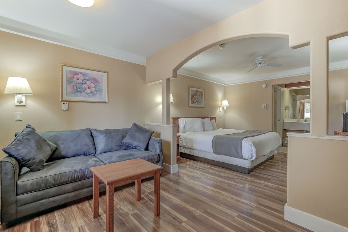 A hotel room with a sofa, a bed, a wooden table, and a ceiling fan.