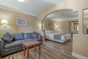 A hotel room with a sofa, a bed, a wooden table, and a ceiling fan. - Shasta Pines Motel & Suites (Burney)