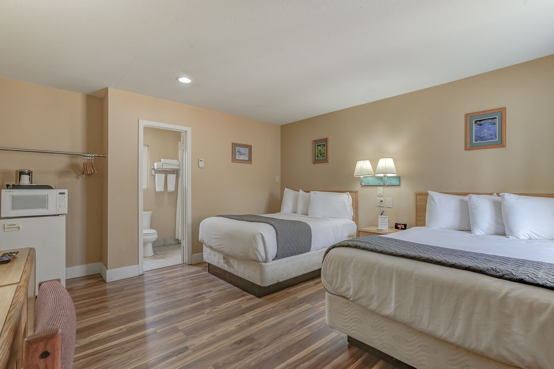 A hotel room with two beds, a microwave, a small table, and a bathroom visible through an open door.