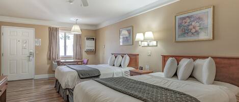 Habitación de hotel con dos camas, ventilador de techo, escritorio, silla, ventana con cortinas y un cuadro en la pared.