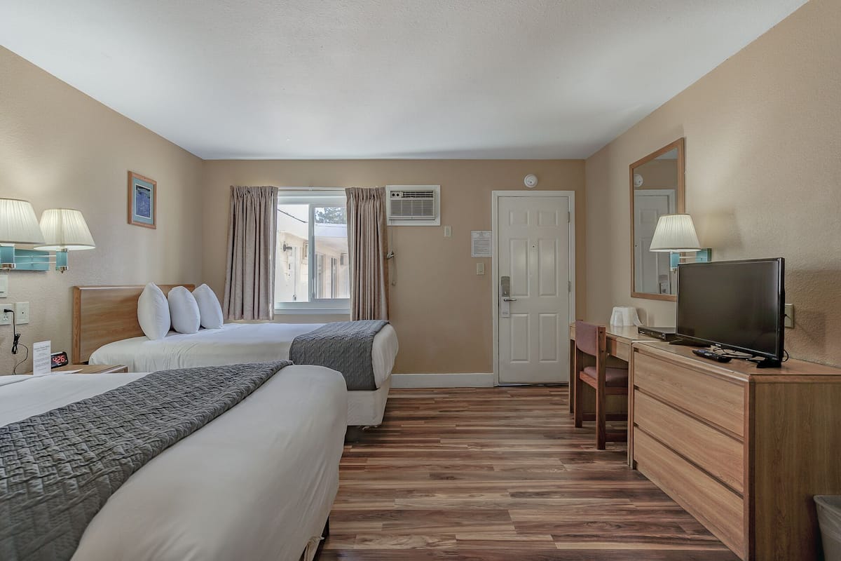 A hotel room with two beds, a desk with a television, a mirror, and a window with curtains.