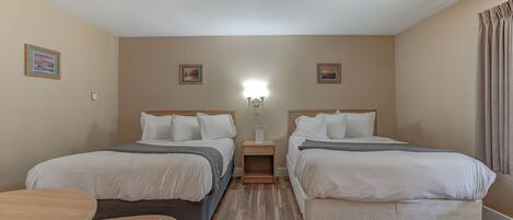A hotel room with two beds, a small table, and a nightstand with a lamp.