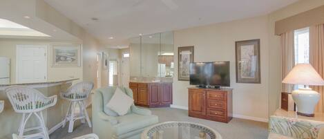 A spacious living room with a ceiling fan, a television, and a dining area with bar stools.