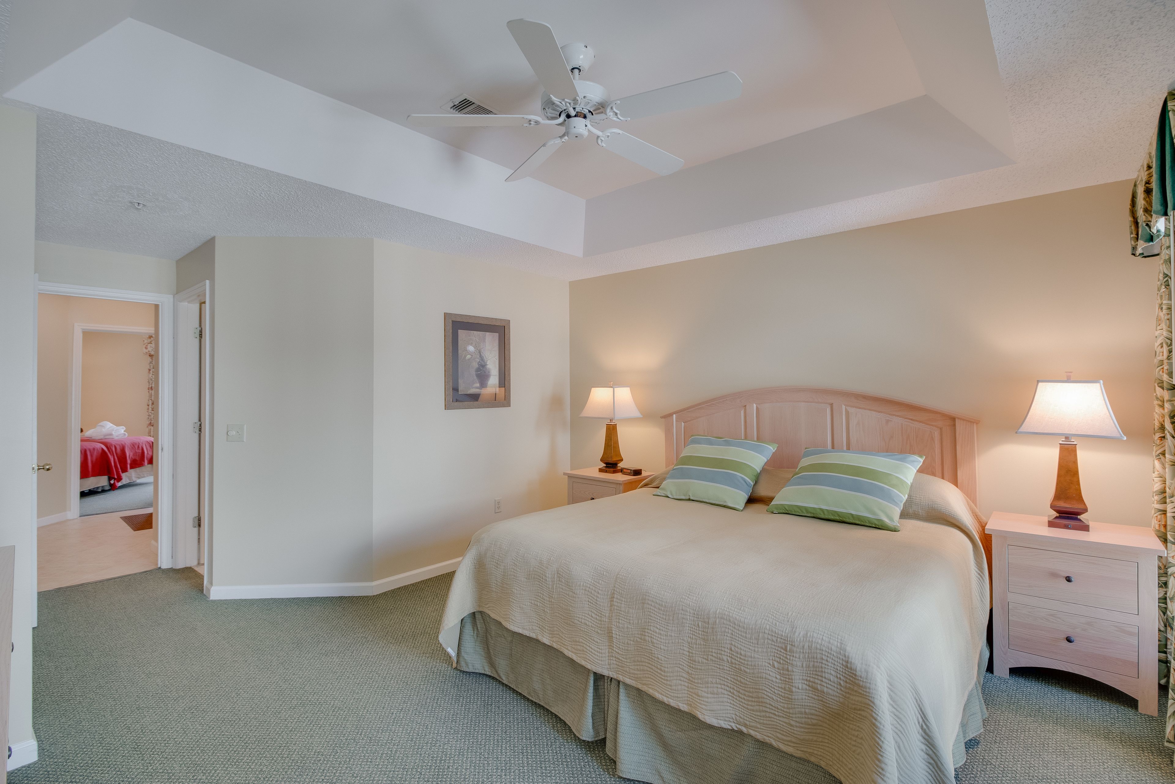A bedroom with a bed, nightstands, a ceiling fan, and a door leading to another room.