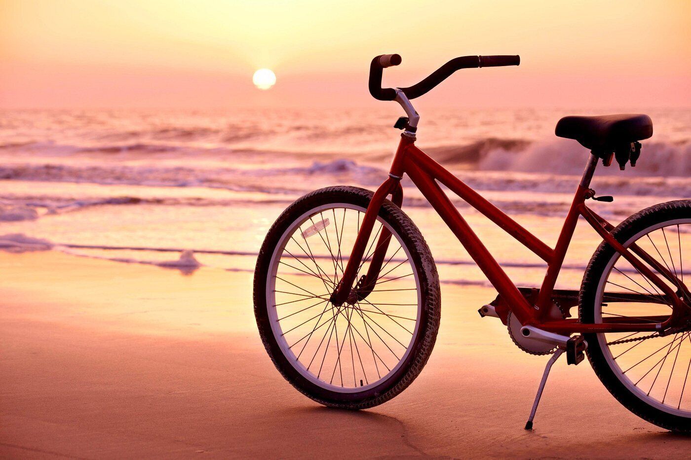 A bicycle parked on a beach with the ocean in the background.