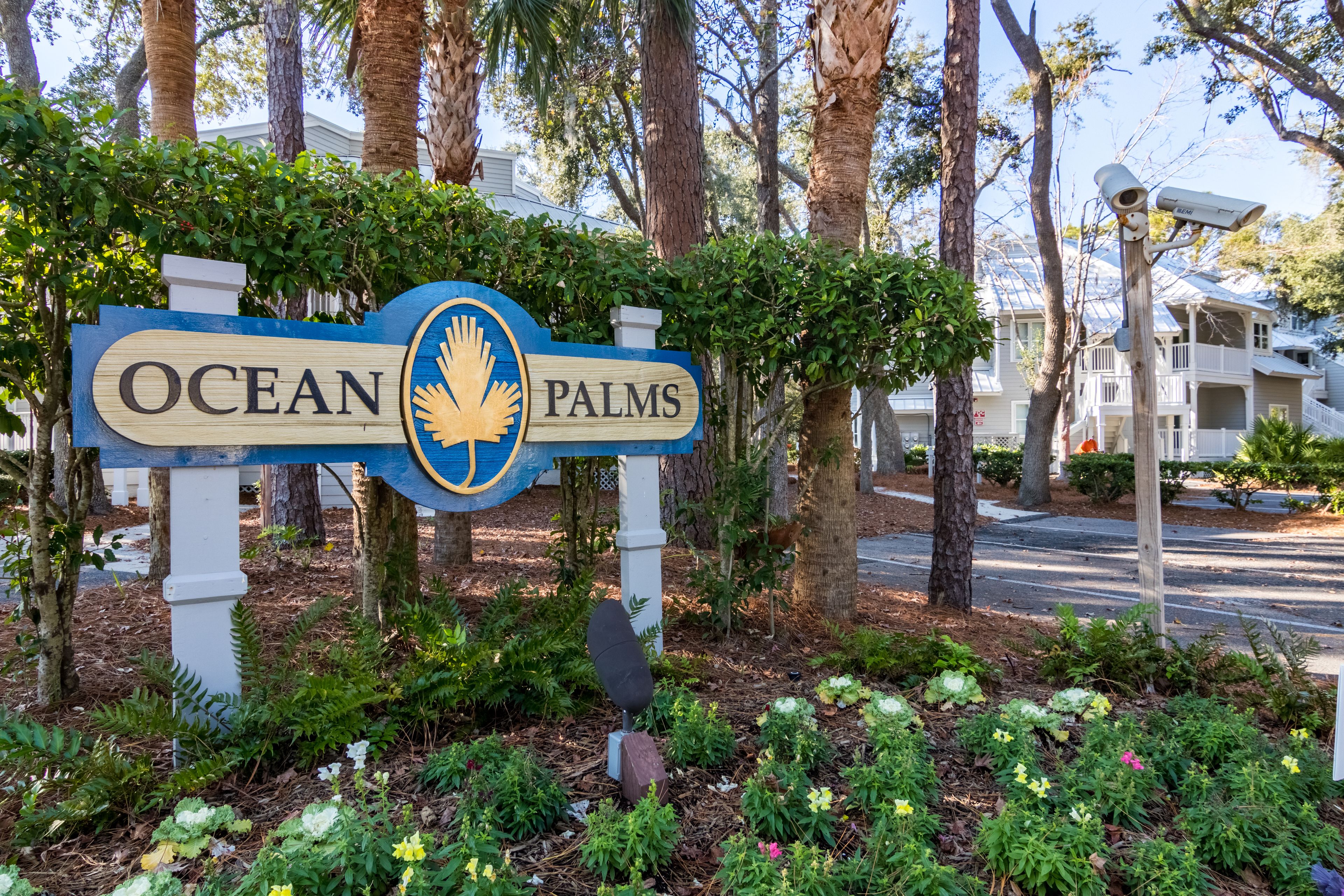 A sign for Ocean Palms with a palm tree and greenery in the background.