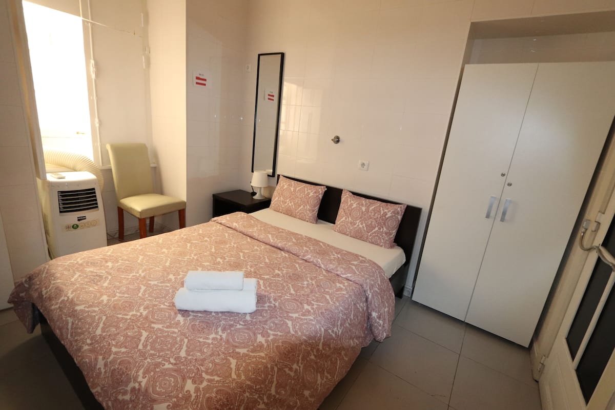 Een hotelkamer met een groot bed, een stoel, een nachtkastje met een lamp, een spiegel en een garderobe.