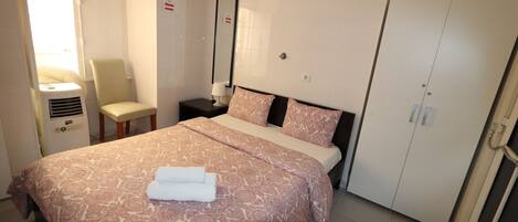 Una habitación de hotel con una cama grande, una silla, una mesita de noche con lámpara, un espejo y un armario.
