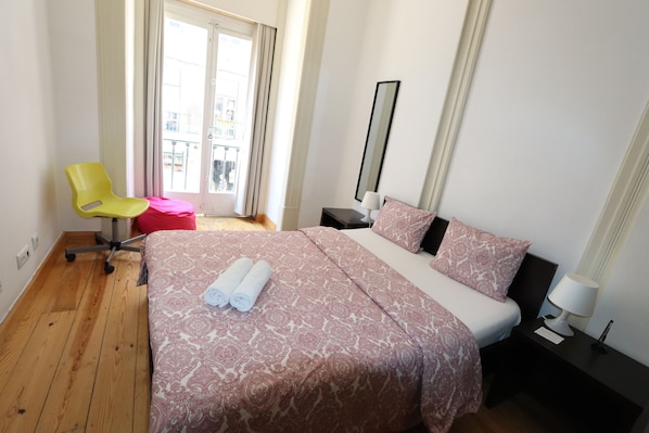 A hotel room with a bed, a chair, a nightstand, and a window with curtains.