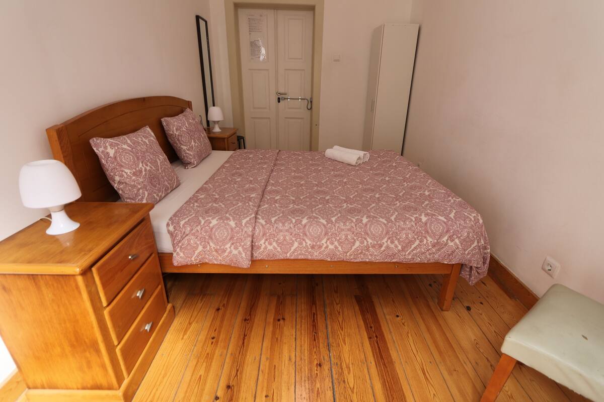 Een slaapkamer met een houten bed, een nachtkastje, een lamp, een kledingkast en een deur.