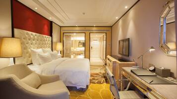 A hotel room with a large bed, a desk with a computer, a chair, a TV, and a bathroom visible through an open door.