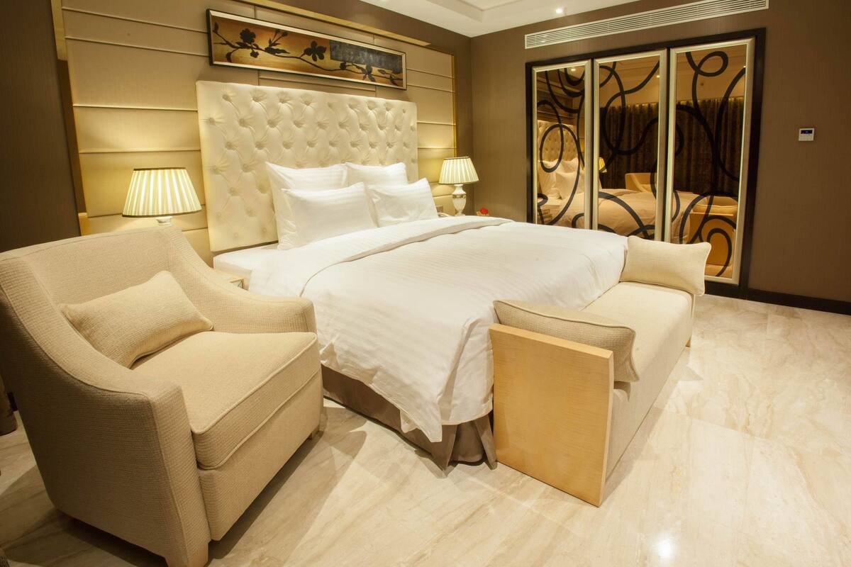 Un dormitorio amplio con una cama grande, dos lámparas de noche, un sofá y un espejo decorativo.