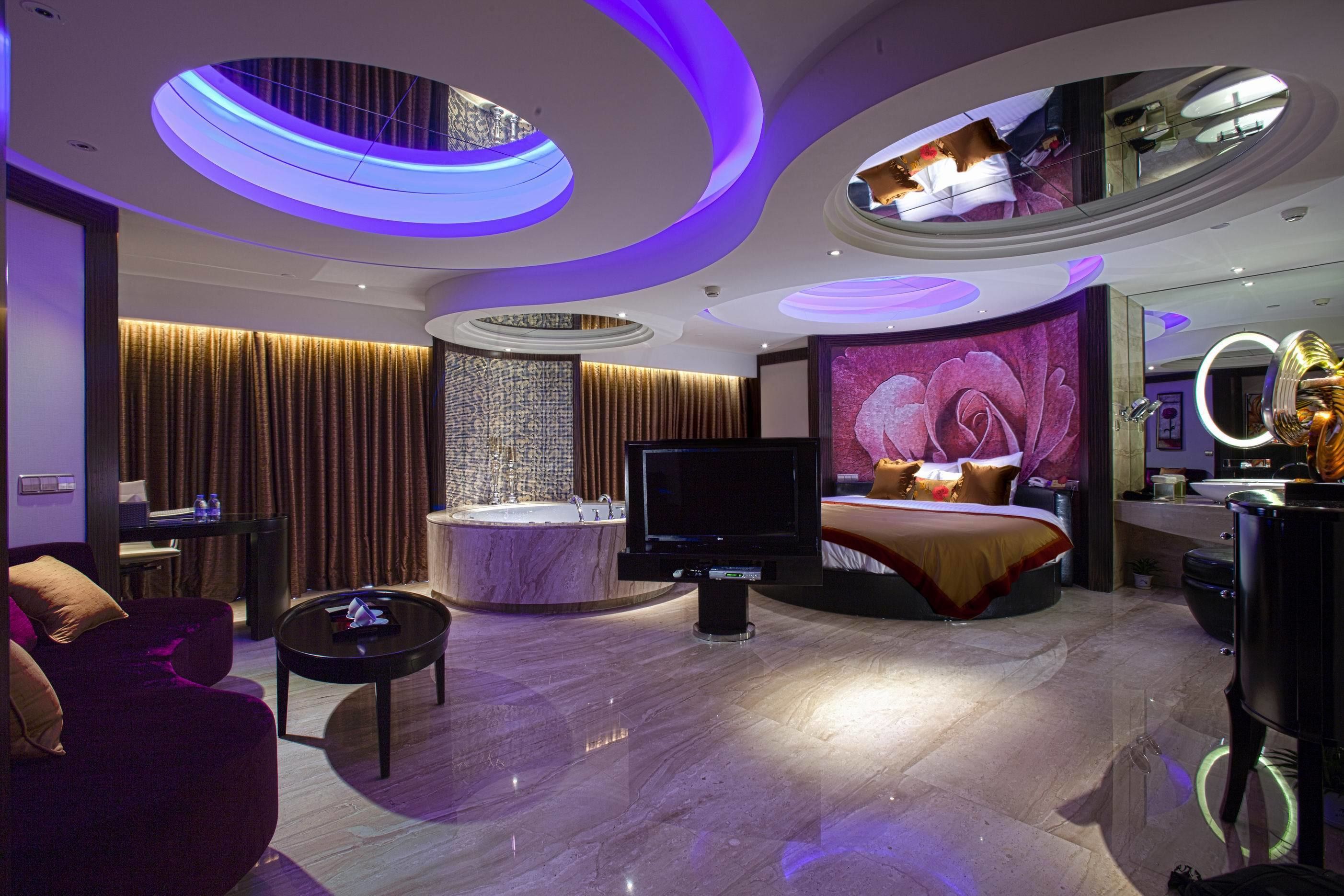 Una camera d'hotel moderna con un letto grande, una TV, un bagno con uno specchio e una zona salotto con un tavolino.
