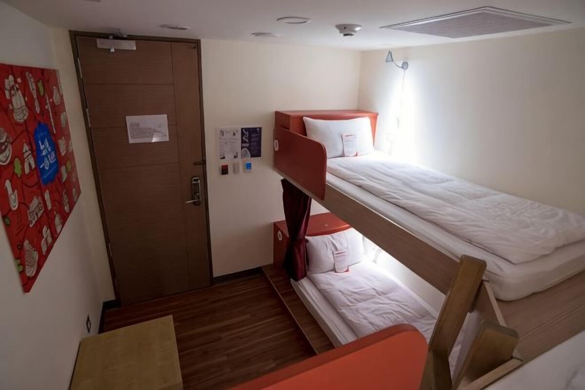 A room with bunk beds, a door, a small table, and a wall decoration.