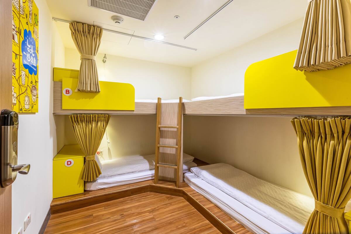 A compact hotel room with bunk beds, a wooden floor, and a yellow accent wall.