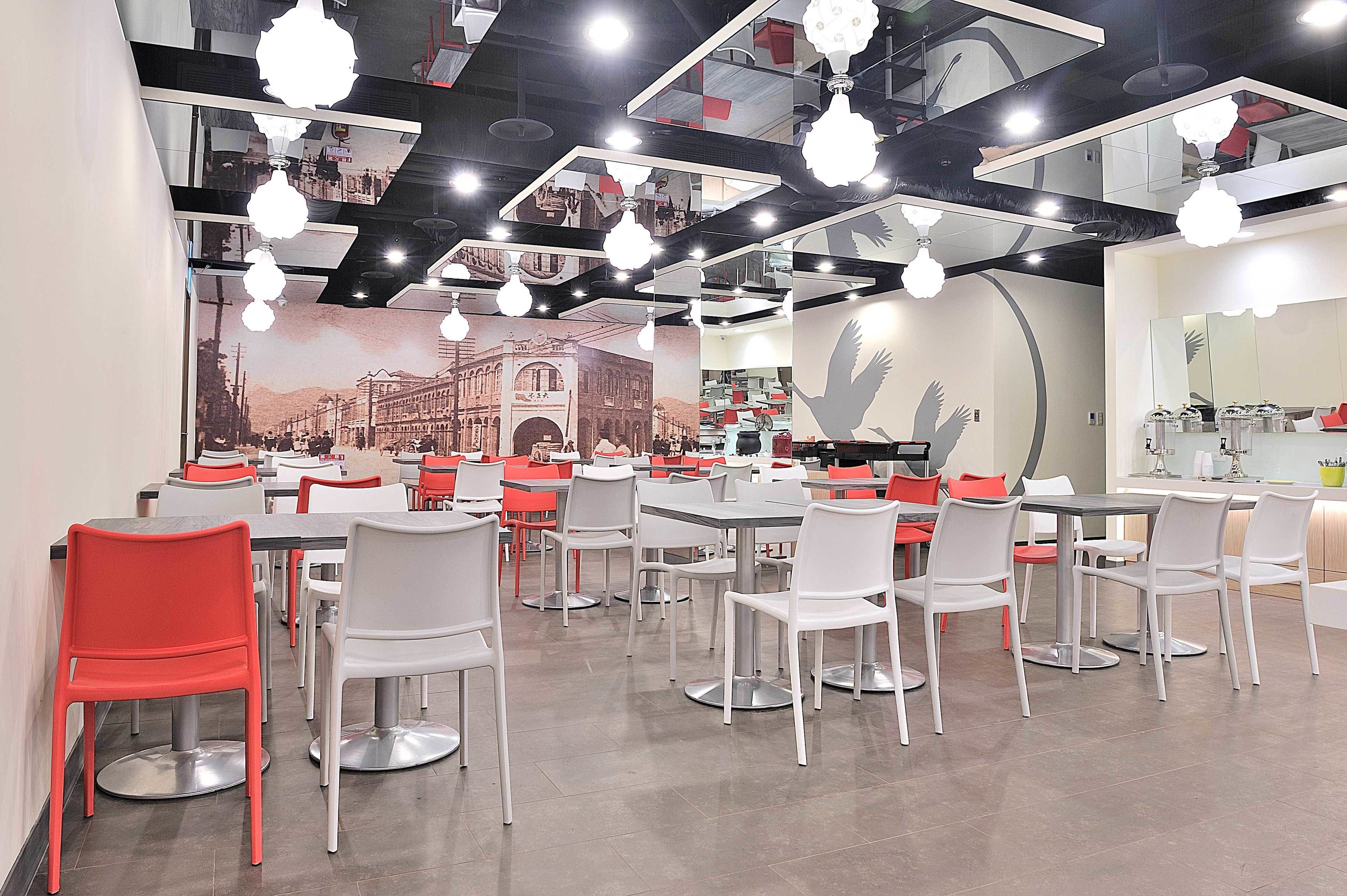 A modern restaurant with multiple dining tables and chairs, a large mural on the wall, and hanging pendant lights.