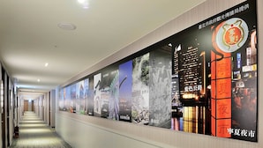 A hotel corridor with a long hallway, posters on the walls, and a patterned carpet. - CU Hotel Taipei (Taipei)