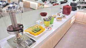 A buffet setup with a juice dispenser, sliced fruits, and various food containers. - CU Hotel Taipei (Taipei)