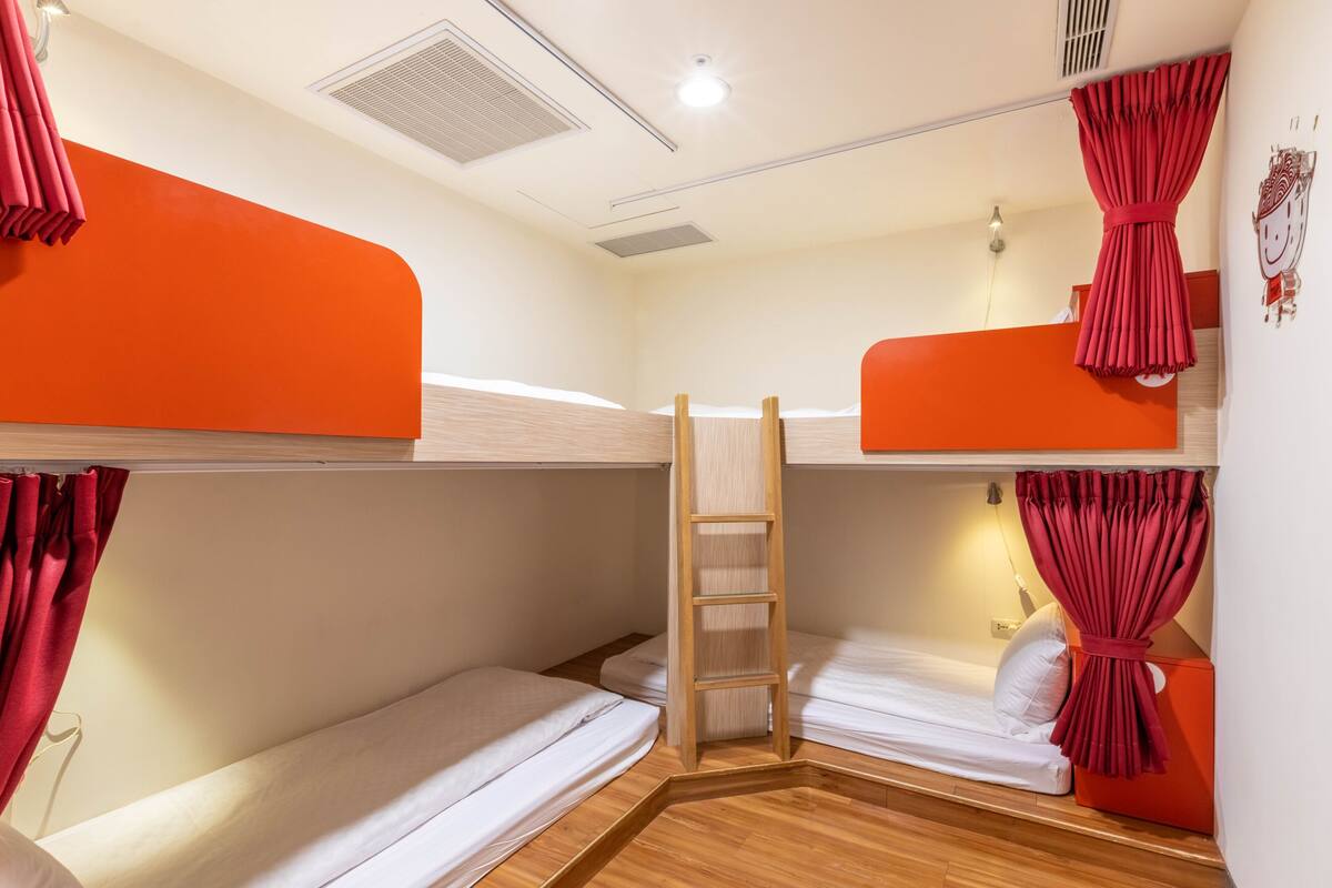 A dormitory room with bunk beds, a wooden ladder, and red curtains.