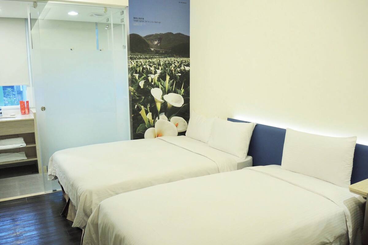 A hotel room with two beds, a desk, and a poster of flowers.