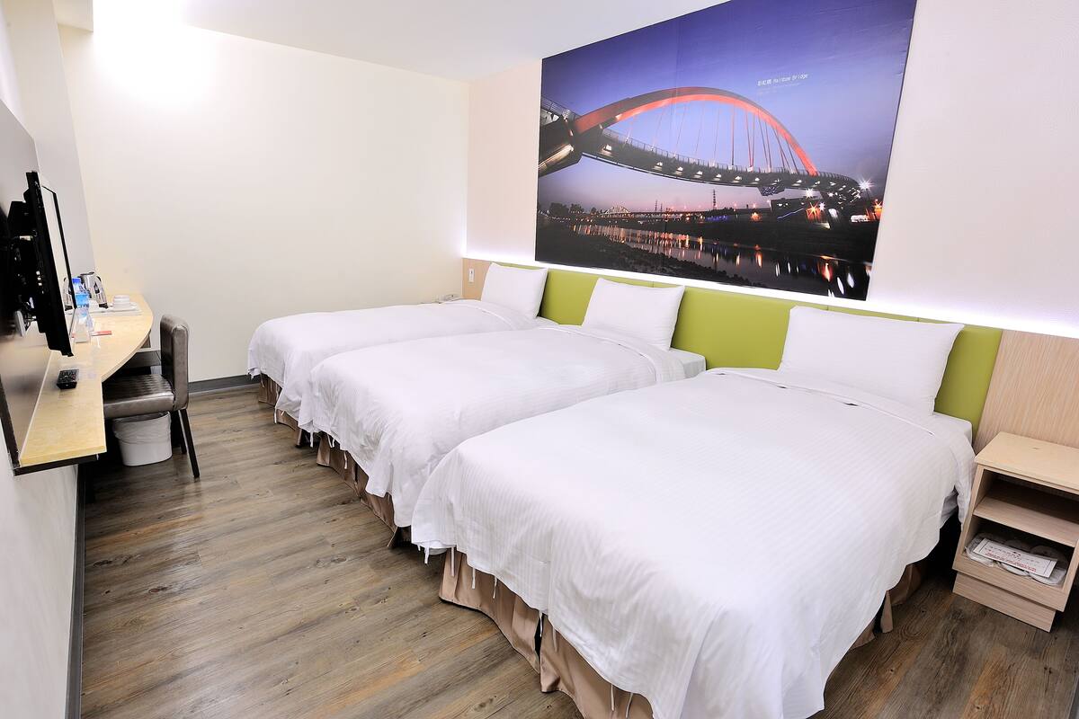 A hotel room with two single beds, a desk with a chair, a small trash bin, and a wall-mounted TV.