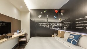 A hotel room with a bed, a desk, a chair, a TV, and a wall with a cityscape and paper airplanes. - CU Hotel Taipei (Taipei)
