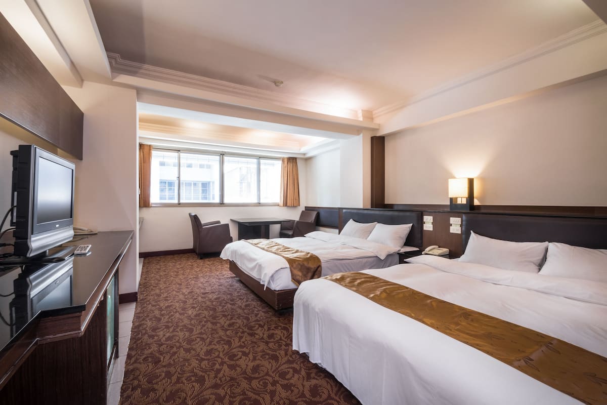 A hotel room with two beds, a desk, a television, and a window with curtains.