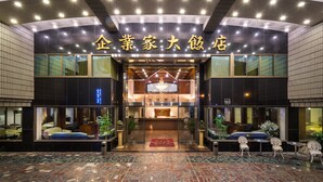 L’entrée d’un hôtel, avec un comptoir d’accueil, un tapis rouge et des espaces aménagés avec des fauteuils.