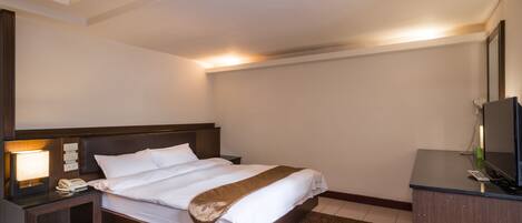 A hotel room with a bed, a nightstand with a lamp, a desk with a computer, and a mirror.