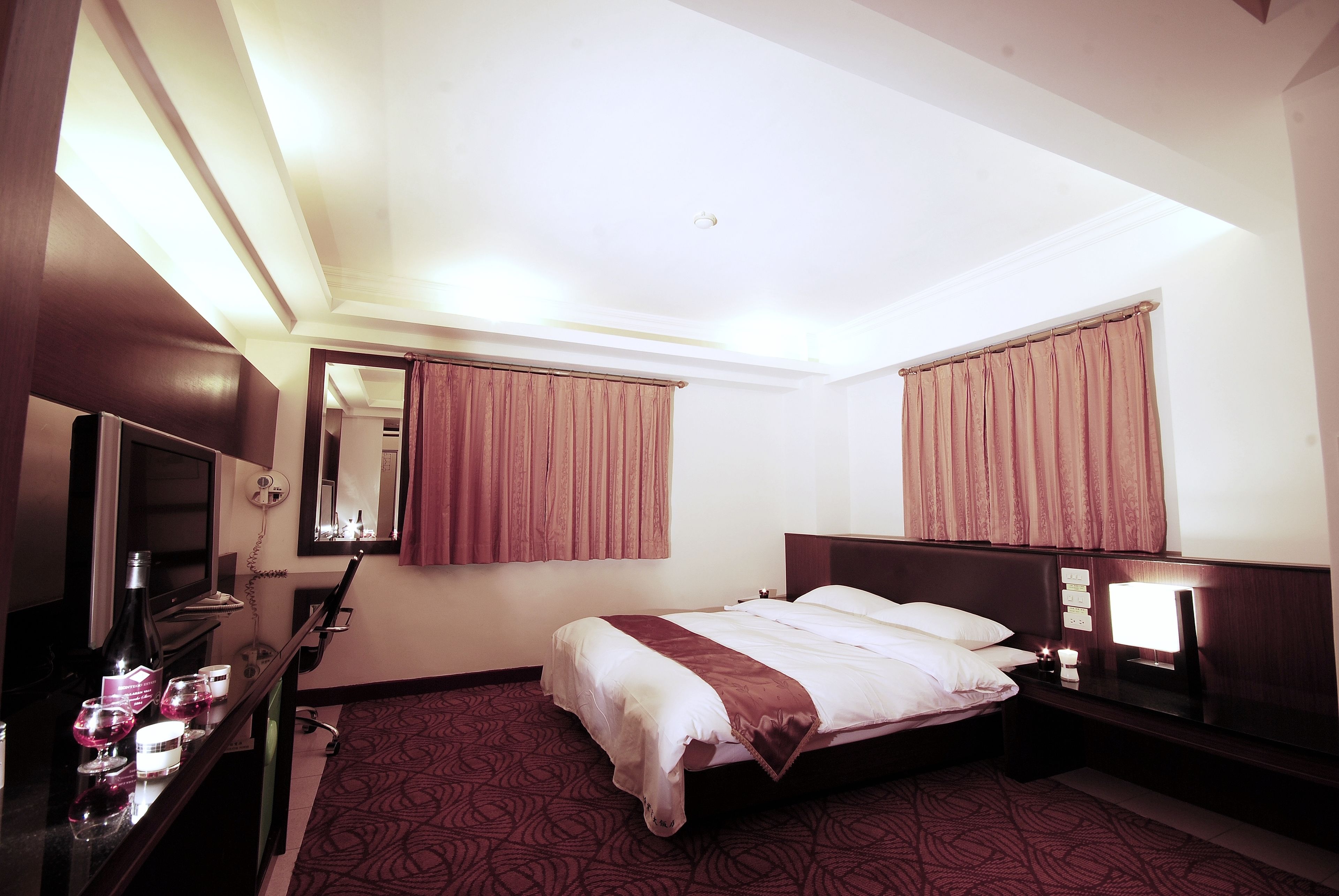 Habitación de hotel con cama, mesita de noche, televisor y espejo.