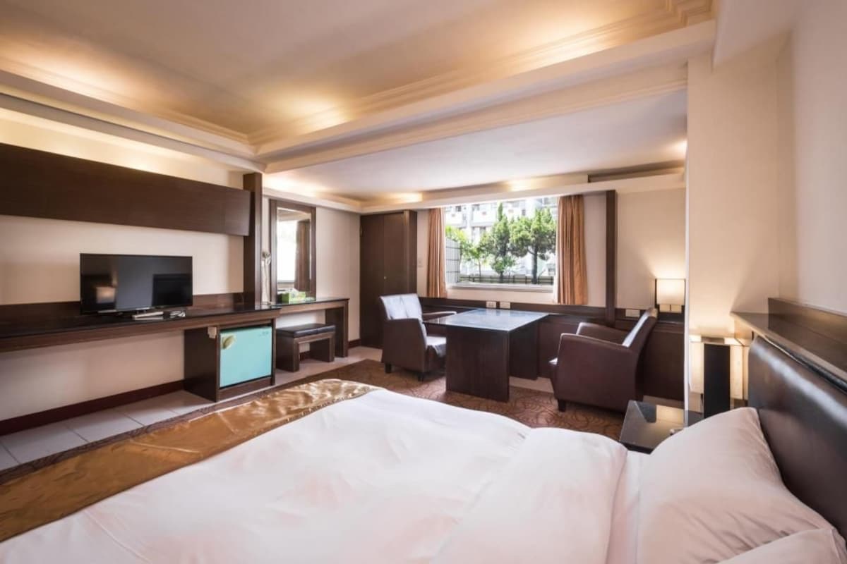 A hotel room with a bed, a desk, a television, and a seating area with chairs.