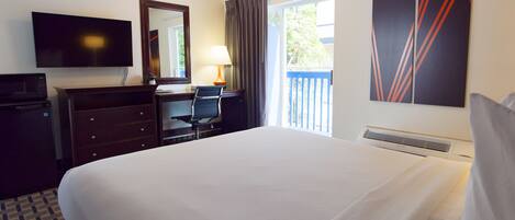 A hotel room with a bed, a desk with a chair, a television, a lamp, and artwork on the wall.