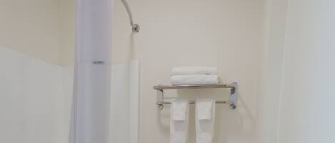 A small bathroom with a bathtub, toilet, and a shelf with towels.