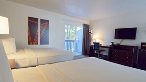 A hotel room with two beds, a desk, a chair, a television, and artwork on the walls.