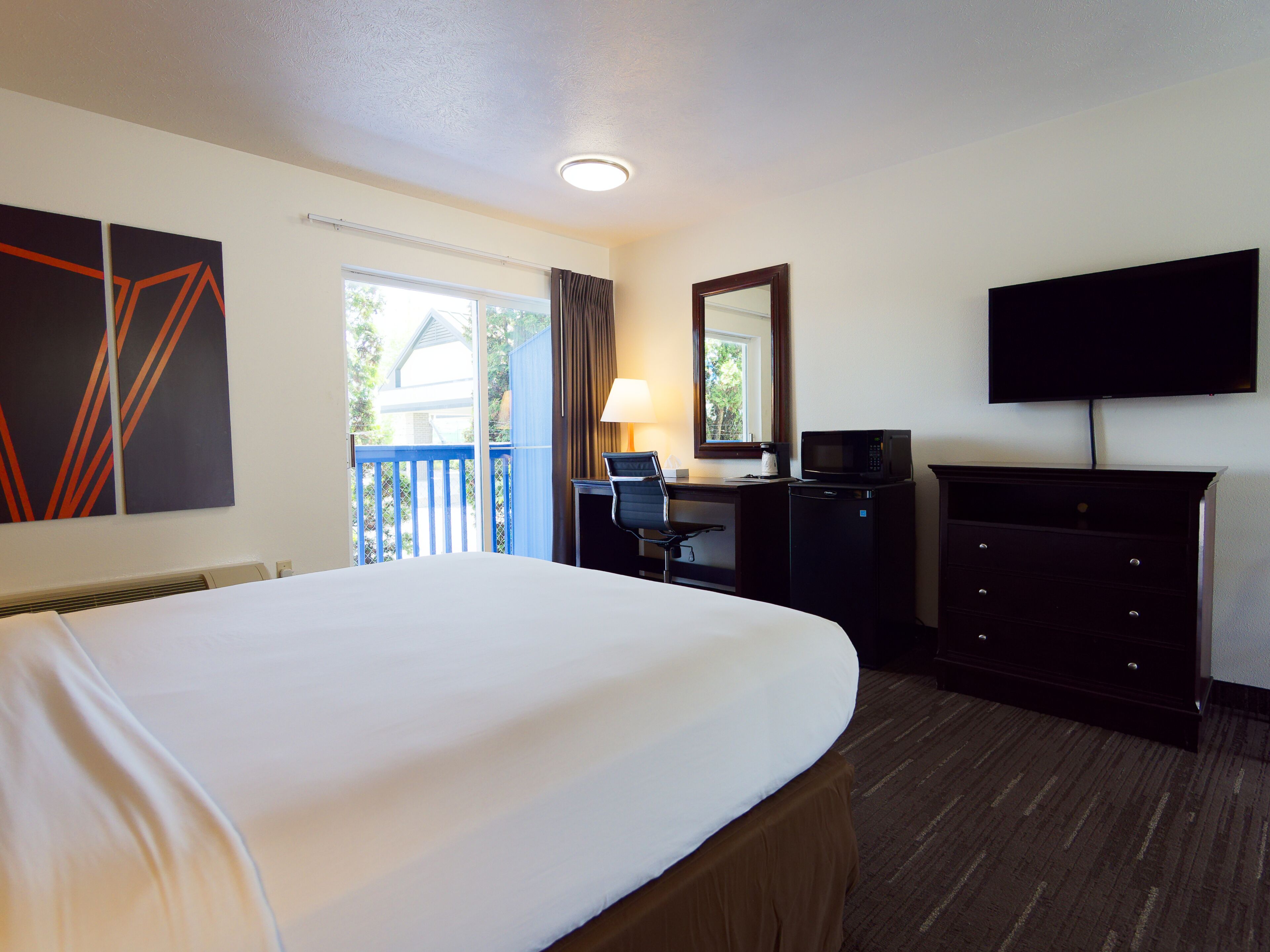 A hotel room with a bed, desk, chair, television, and a view of the outdoors.