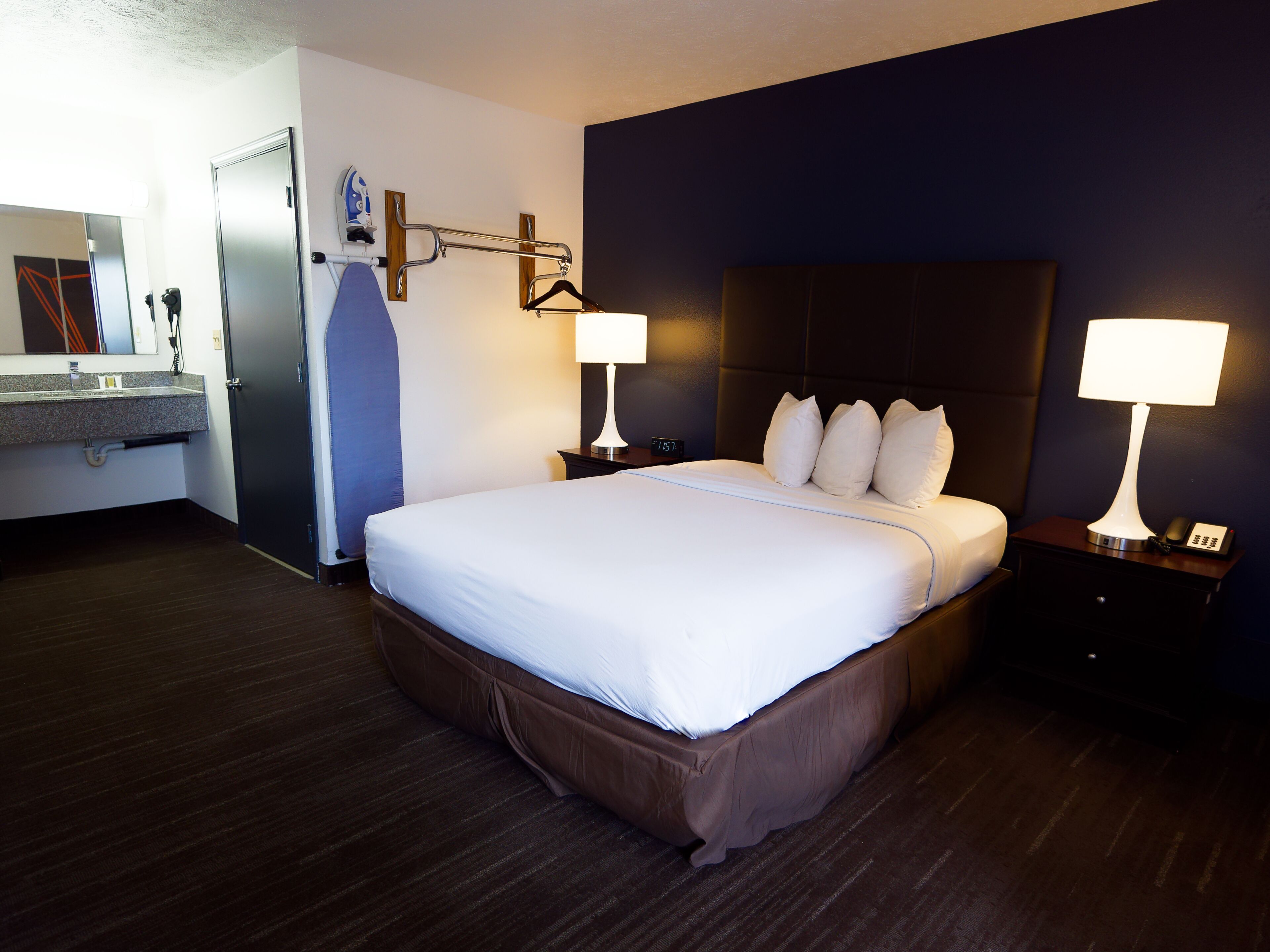 Ein Hotelzimmer mit einem großen Bett, Nachttischlampen, einem Nachttisch, einem Schminktisch und einem Handtuchhalter.