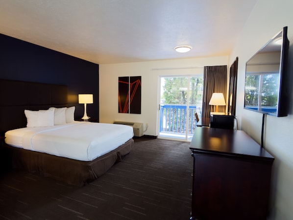 A hotel room with a large bed, a desk, a TV, a window with curtains, and a door leading to a balcony.