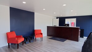 A reception area with a dark wooden desk, two red chairs, and a light-colored wooden floor.