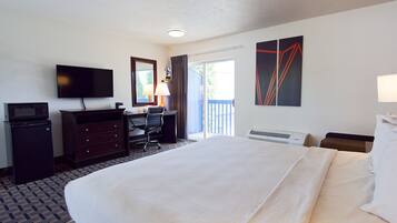 Habitación de hotel con cama, escritorio con silla, televisor, microondas, cómoda y ventana con cortinas.
