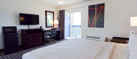 A hotel room with a bed, a desk with a chair, a television, a microwave, a dresser, and a window with curtains.